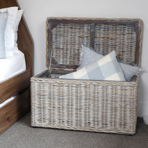 Greywash rattan storage trunk beside a bed with its hinged lid open