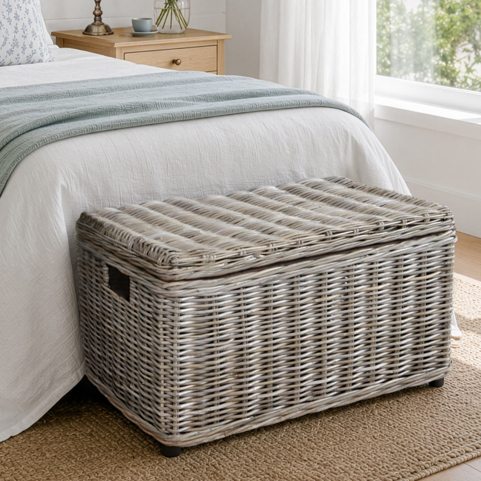 Greywash woven rattan blanket box positioned beside a bed on a patterned rug