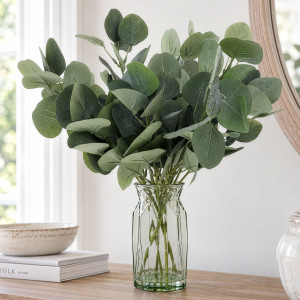 Green artificial eucalyptus arrangement in a faceted glass vase on a wooden console