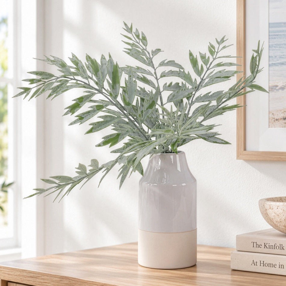Soft green artificial fern arrangement in a grey and cream ceramic vase on a console