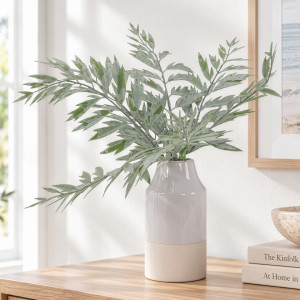 Soft green artificial fern arrangement in a grey and cream ceramic vase on a console