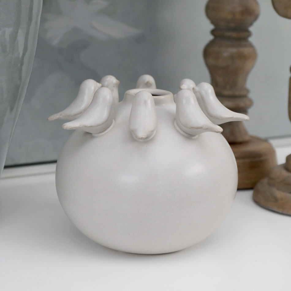 Round off-white ceramic vase with sculpted birds around the rim styled beside a natural wood candlestick.