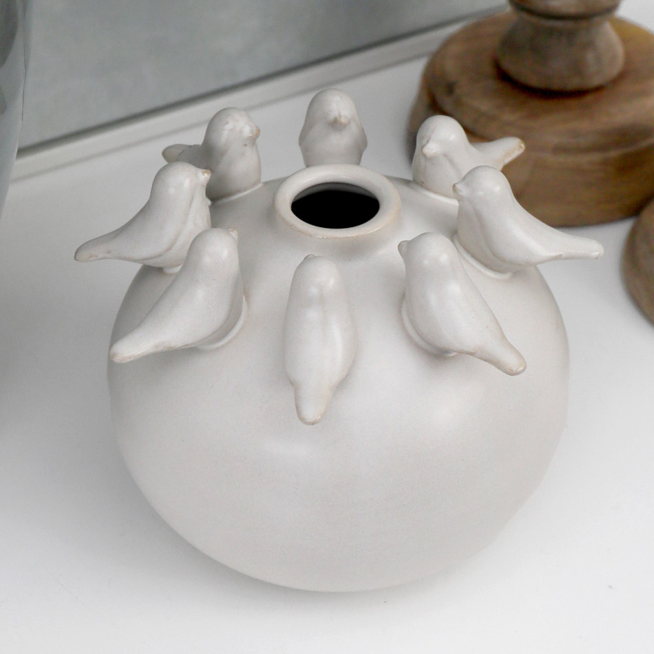 Close-up of an off-white round ceramic vase with small sculpted birds circling the top opening.
