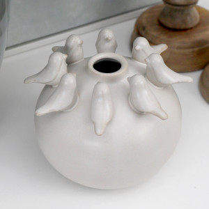 Close-up of an off-white round ceramic vase with small sculpted birds circling the top opening.