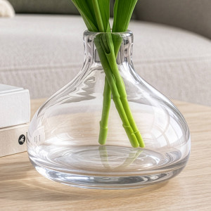 Close-up of a low clear glass vase holding green flower stems in water
