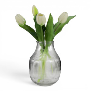 Rounded ribbed glass vase holding four white tulips against a white background