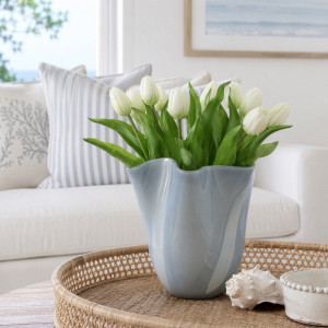 Sea grey waved glass vase filled with white tulips on a woven coffee table tray