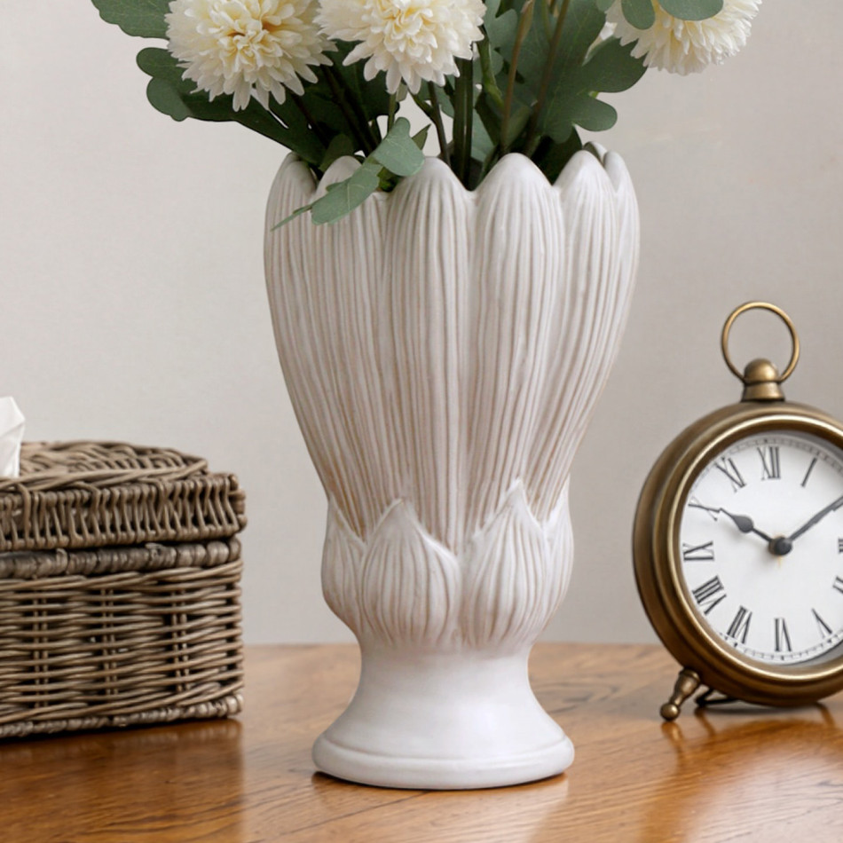 Cream sculpted tulip vase filled with white pom-pom flowers beside a brass clock