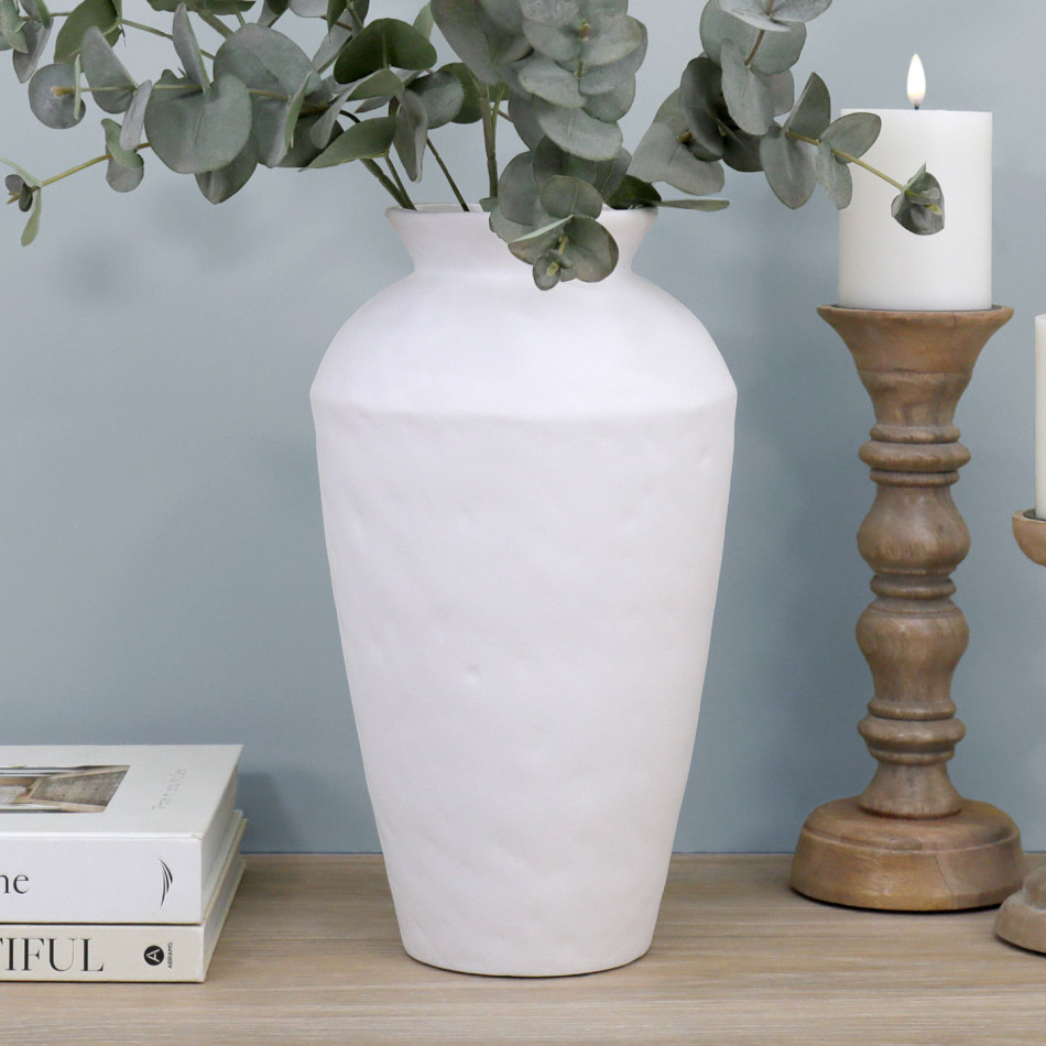 Tall matt white ceramic vase with eucalyptus stems styled beside a natural wood candleholder.