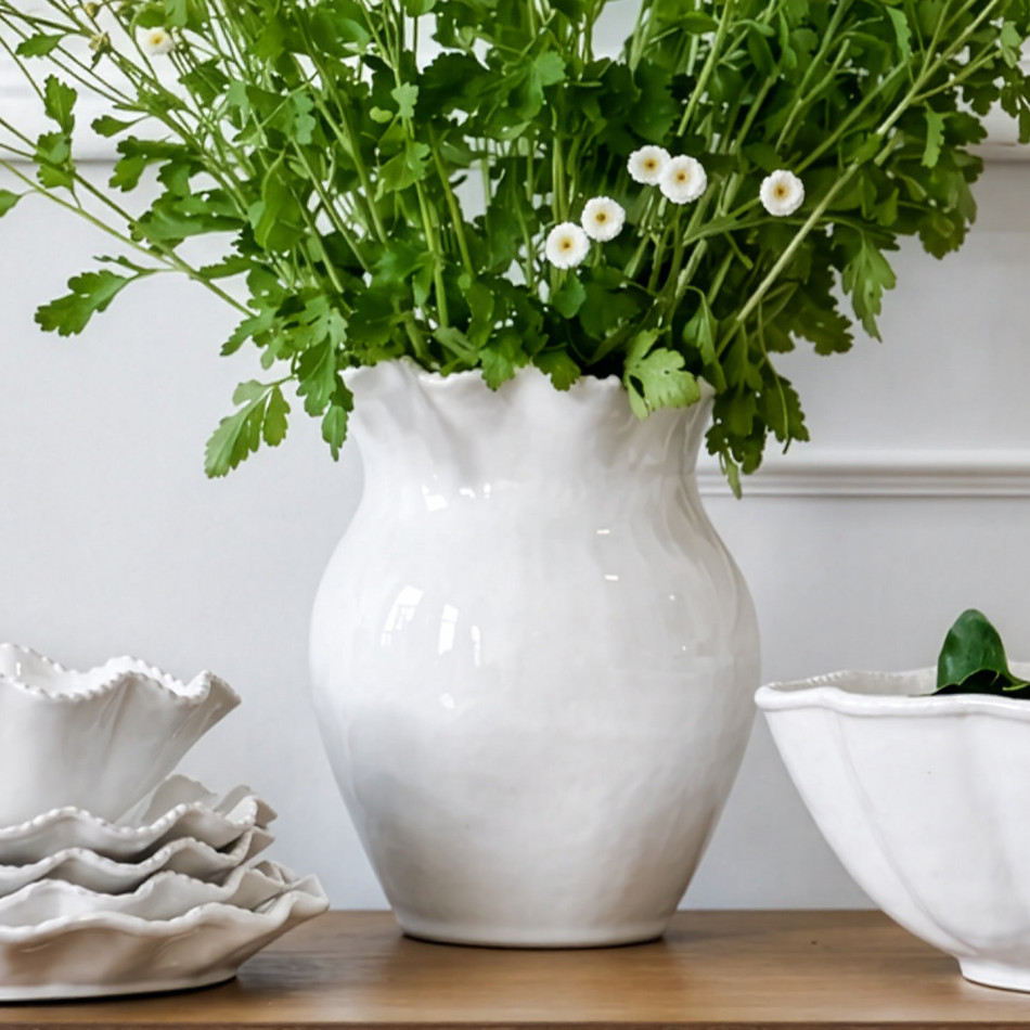 White ceramic rope-rim vase filled with green foliage and small white flowers