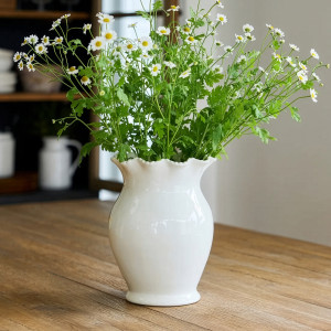 White rope-rim ceramic vase holding a loose arrangement of daisies on a timber table