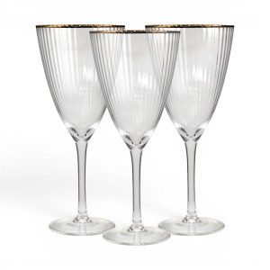 Three clear ribbed wine glasses with gold-coloured rims and tall stems against a white background
