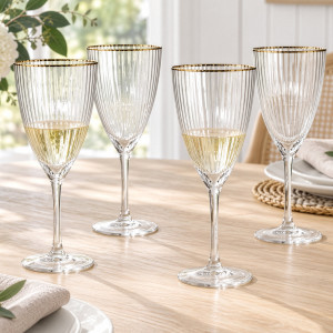 Four ribbed wine glasses with gold-coloured rims on a timber dining table, two holding white wine