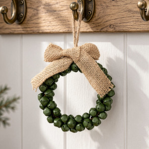 Close-up of green metal jingle bell wreath with hessian bow hanging from a hook on a wooden coat rack